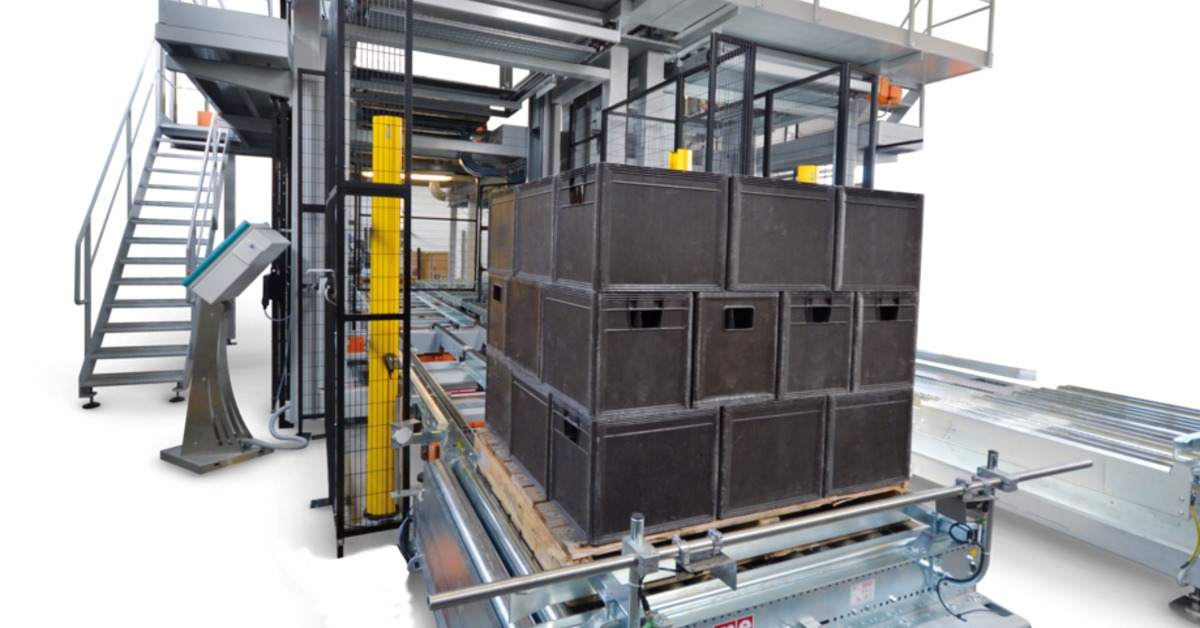 Black plastic crates are stacked in three layers on a wooden pallet inside the OCME Antares depalletizer.